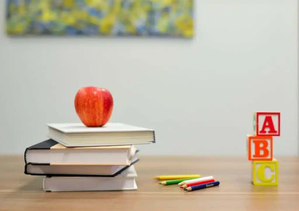 aaron-burden-QJDzYT_K8Xg-unsplash An open book and a notebook with a pen on a table, with a bookshelf in the background.